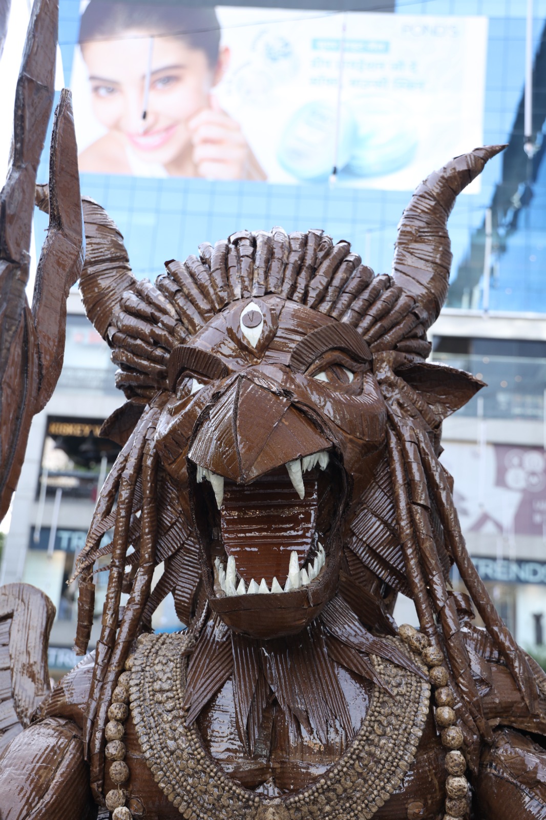Three-quarter close-up of the fierce roaring face of Narasimha, featuring fluted cardboard horns, white teeth, and third eye.