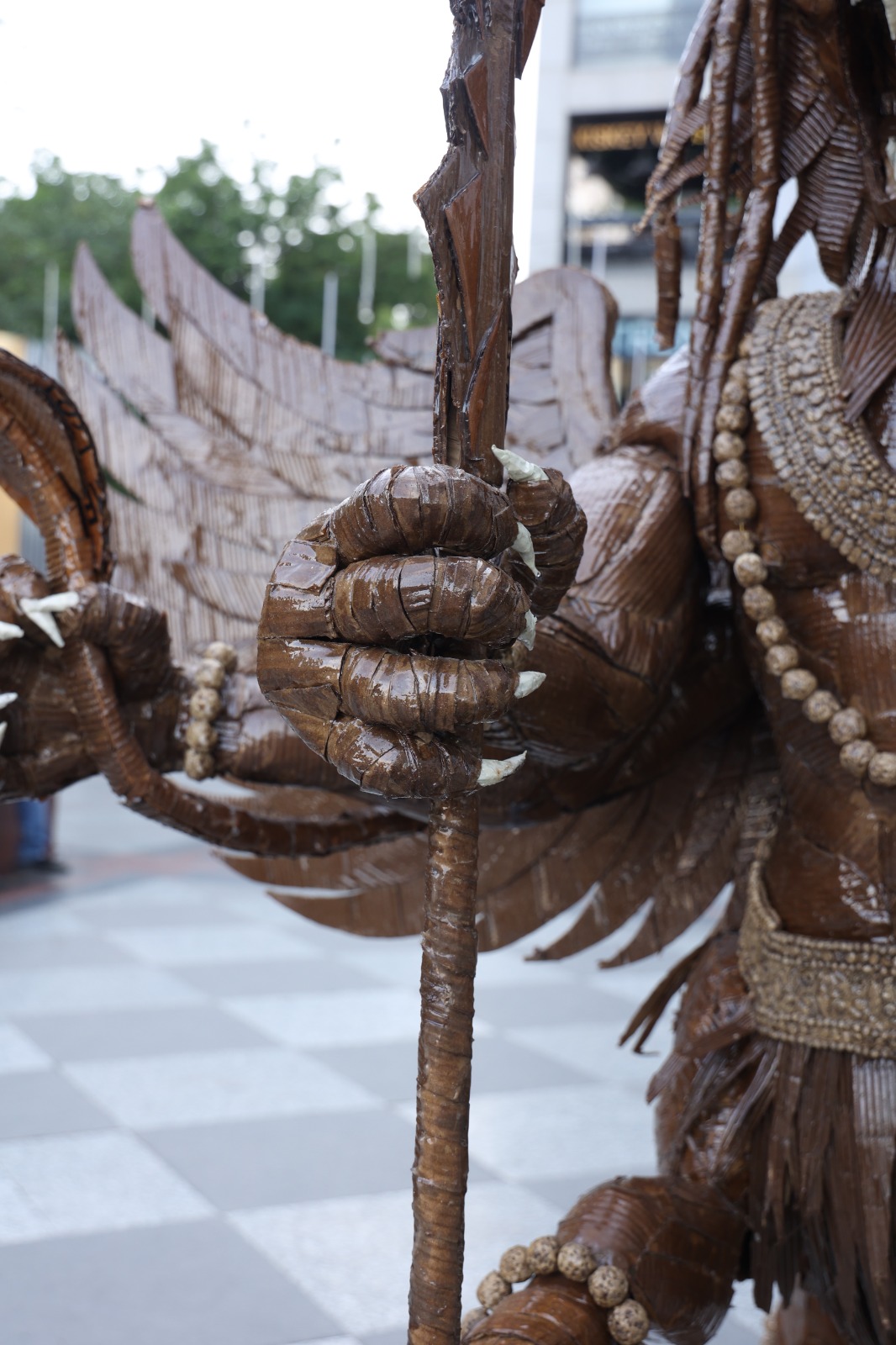 Close-up of clawed hand with white talons gripping the spiral-wrapped shaft of the cardboard trishula trident.